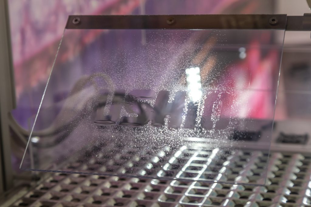 This polymer substrate was masked with a metal USHIO stencil then had excimer light projected through onto the substrate. When water is sprayed on to the irradiated surface, the water clings to the USHIO logo with a surface contact angle of 0 degrees.